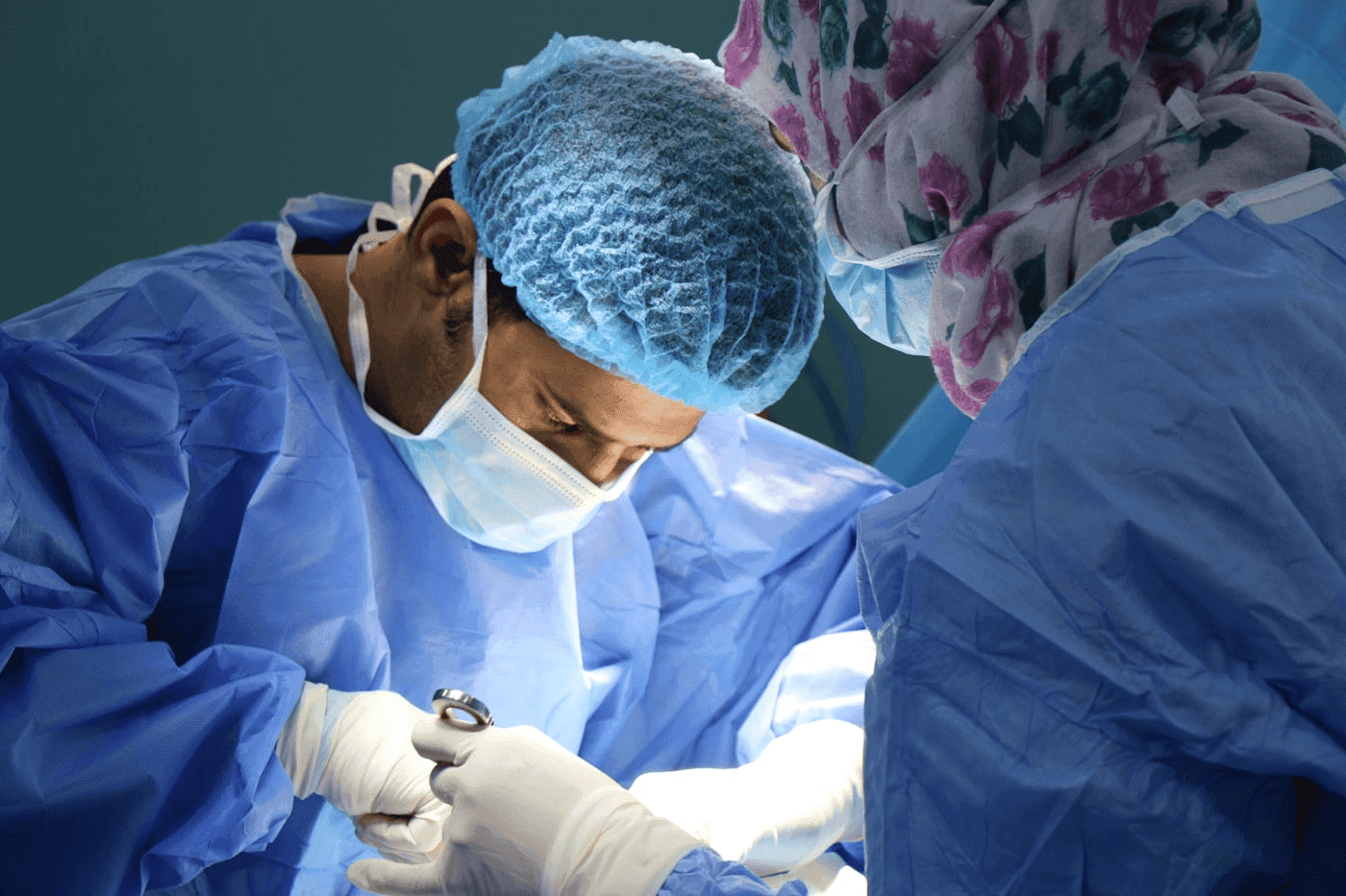 Two surgeons in sterile gowns performing a procedure under bright operating lights